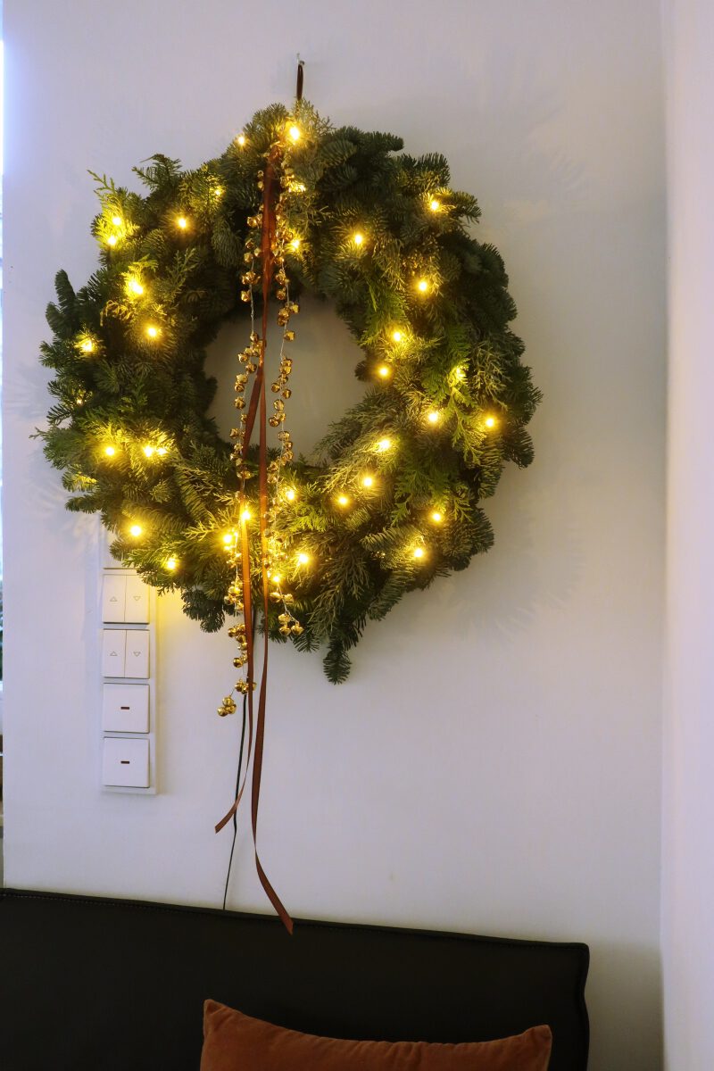 Weihnachtlich dekorieren: Ein Kranz aus Tannengrün mit goldenen Glöckchen und Lichterkette sorgt für weihnachtliche Stimmung.