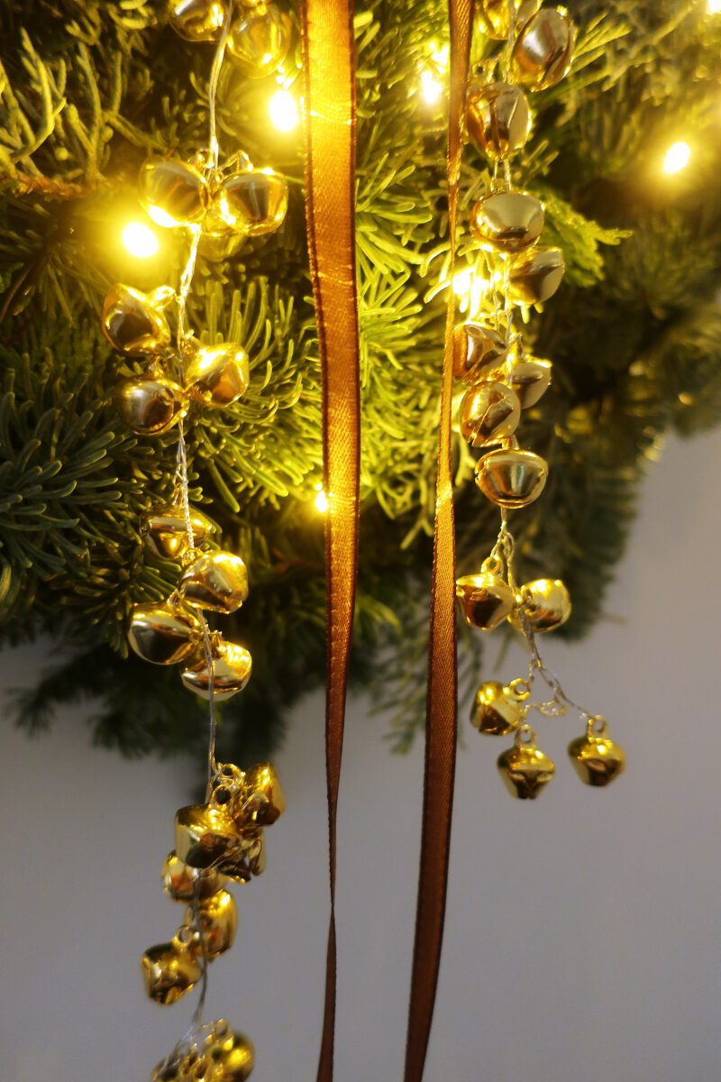 Weihnachtlich dekorieren: Ein Kranz aus Tannengrün mit goldenen Glöckchen und Lichterkette sorgt für weihnachtliche Stimmung.