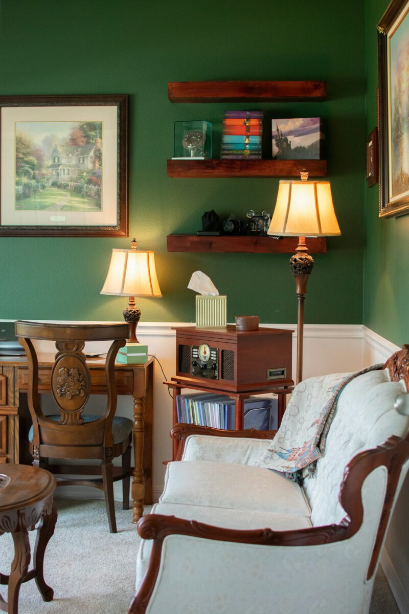 Ein Sofa im Biedermeier-Stil mit hellem Bezug in einem Zimmer voller Möbel und grüner Wandfarbe